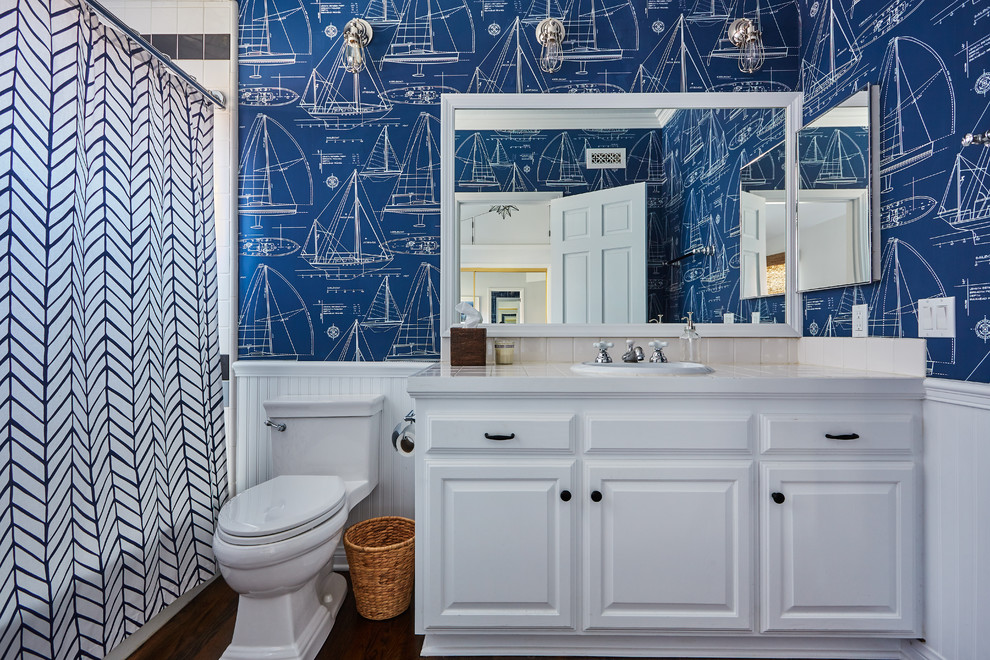 Mid-sized elegant kids' beige tile medium tone wood floor bathroom photo in Orange County with raised-panel cabinets, white cabinets, blue walls, a drop-in sink and tile countertops
