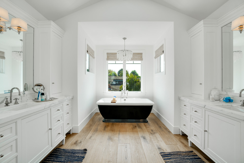 Пример оригинального дизайна: большая главная ванная комната в морском стиле с белыми фасадами, отдельно стоящей ванной, светлым паркетным полом, врезной раковиной, мраморной столешницей, белой столешницей и фасадами с декоративным кантом