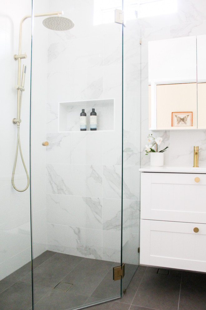 Cette image montre une petite salle d'eau minimaliste avec un placard à porte shaker, des portes de placard blanches, une douche d'angle, WC à poser, un carrelage blanc, des carreaux de céramique, un mur blanc, un sol en carrelage de porcelaine, un lavabo intégré, un plan de toilette en surface solide, un sol gris, une cabine de douche à porte battante, un plan de toilette blanc, une niche, meuble simple vasque et meuble-lavabo suspendu.