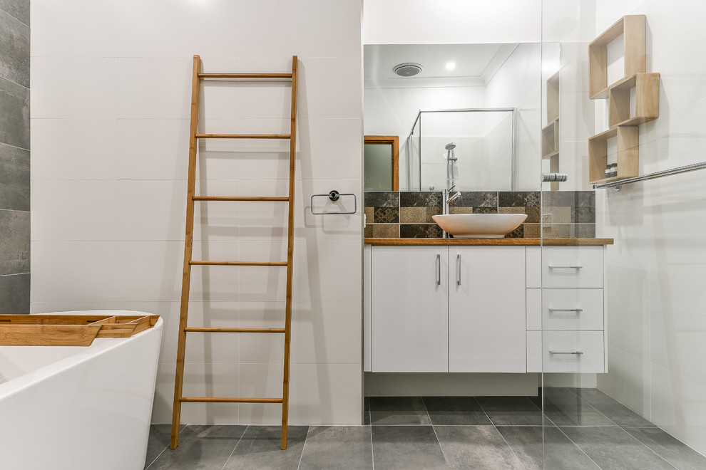 Réalisation d'une salle de bain design avec un placard à porte plane, des portes de placard blanches, une baignoire indépendante, un mur blanc, une vasque et un sol gris.