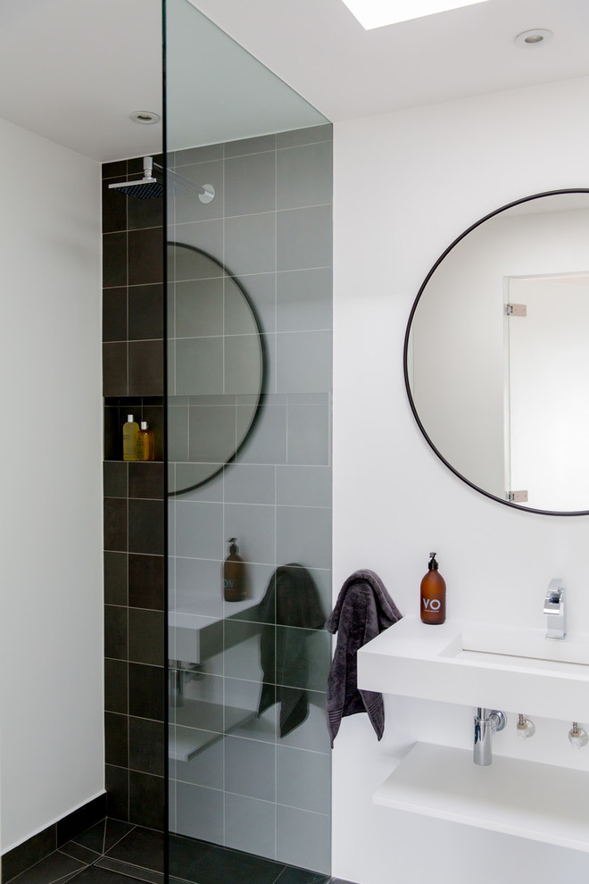 This is an example of a large contemporary ensuite bathroom in London with recessed-panel cabinets, a walk-in shower, a wall mounted toilet, white walls, ceramic flooring, a wall-mounted sink and black floors.