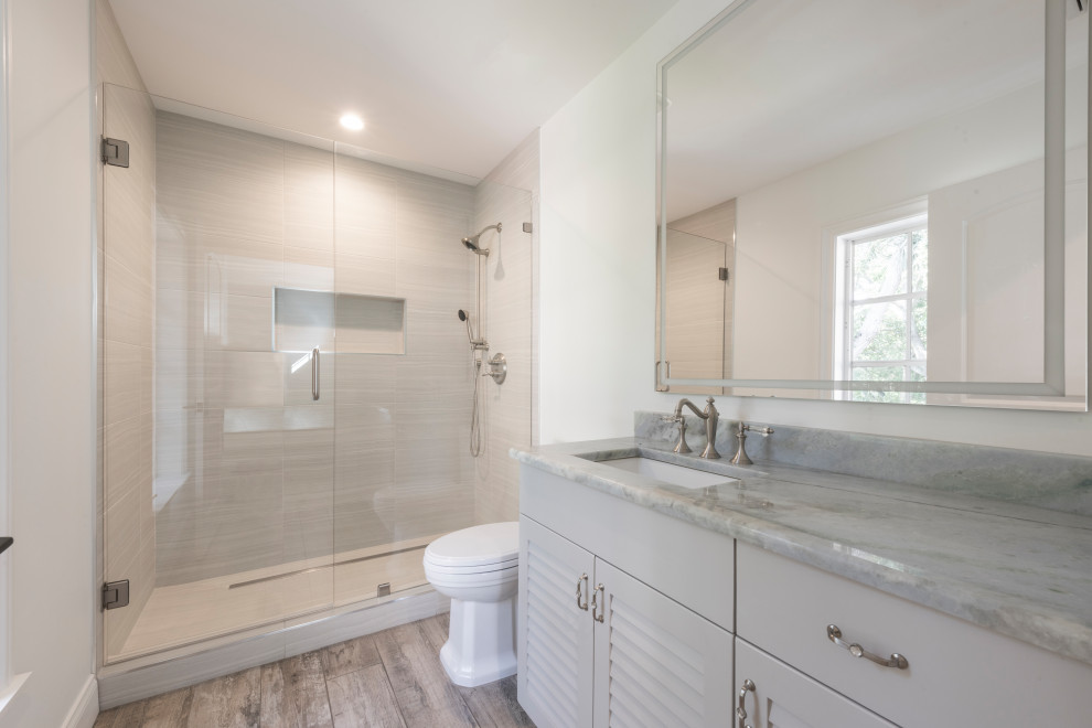 Large trendy master vinyl floor, brown floor and double-sink bathroom photo in Tampa with beaded inset cabinets, medium tone wood cabinets, a one-piece toilet, an undermount sink, quartz countertops, a hinged shower door, multicolored countertops and a built-in vanity