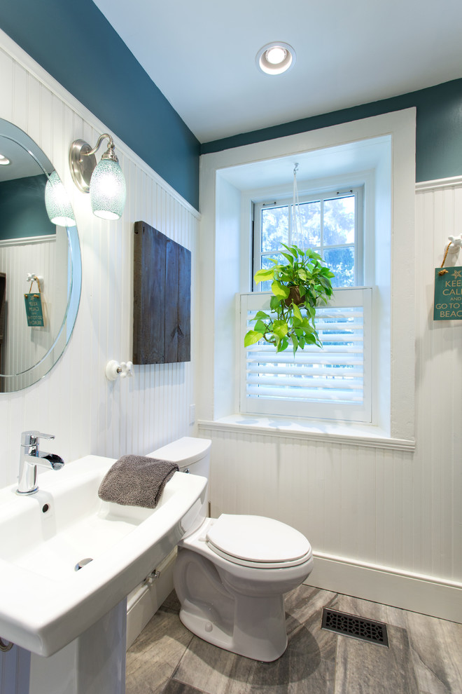 Modelo de cuarto de baño costero de tamaño medio con paredes multicolor, suelo de baldosas de porcelana, lavabo con pedestal, encimera de vidrio, sanitario de dos piezas y ducha esquinera