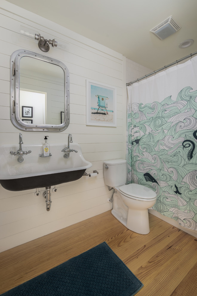 Coastal family bathroom in Charleston with an alcove bath, a shower/bath combination, a two-piece toilet, white walls, light hardwood flooring, a trough sink, beige floors and a shower curtain.