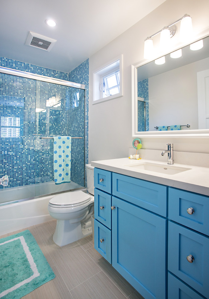 На фото: детская ванная комната среднего размера в классическом стиле с врезной раковиной, фасадами в стиле шейкер, синими фасадами, столешницей из искусственного кварца, ванной в нише, синей плиткой, плиткой мозаикой, полом из керамогранита, угловым душем, бежевыми стенами, раздельным унитазом, серым полом и серой столешницей с