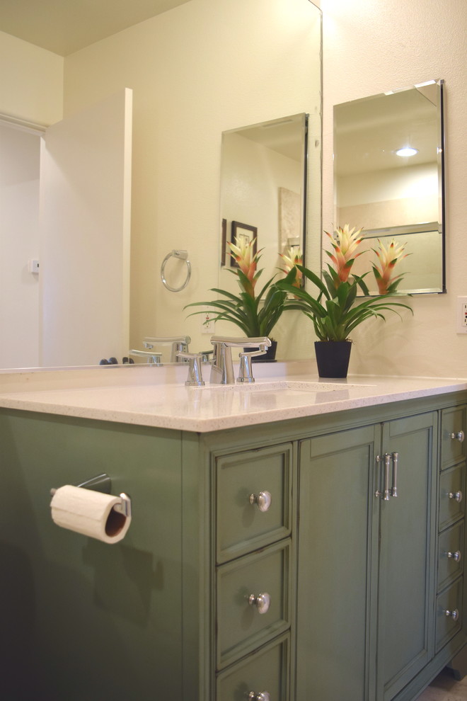 This is an example of a medium sized beach style ensuite bathroom in Santa Barbara with recessed-panel cabinets, green cabinets, a built-in bath, a shower/bath combination, a two-piece toilet, beige tiles, stone slabs, white walls, marble flooring, a submerged sink and marble worktops.