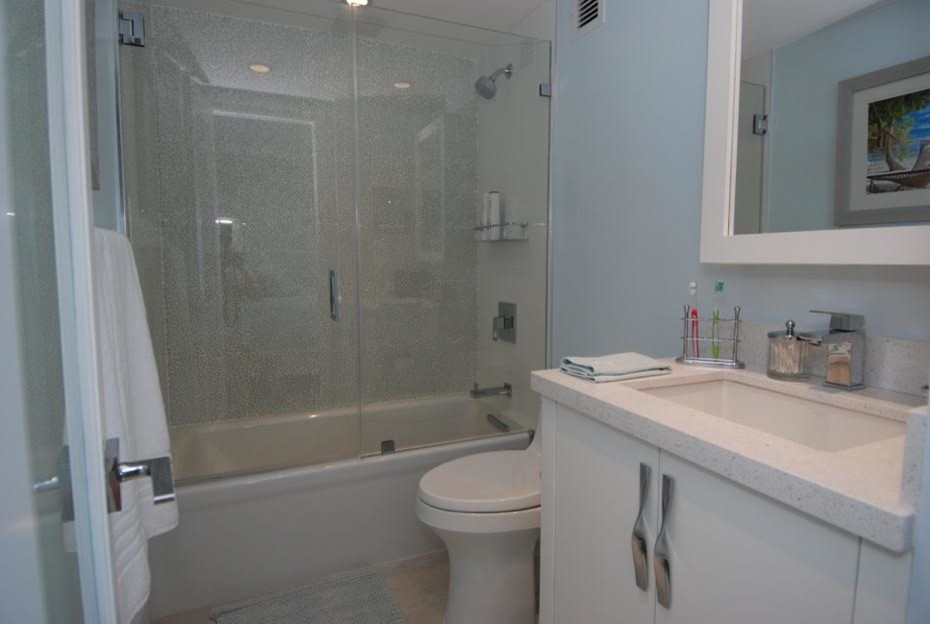 Пример оригинального дизайна: ванная комната среднего размера в морском стиле с плоскими фасадами, белыми фасадами, ванной в нише, душем в нише, бежевой плиткой, каменной плиткой, душевой кабиной и столешницей из искусственного кварца