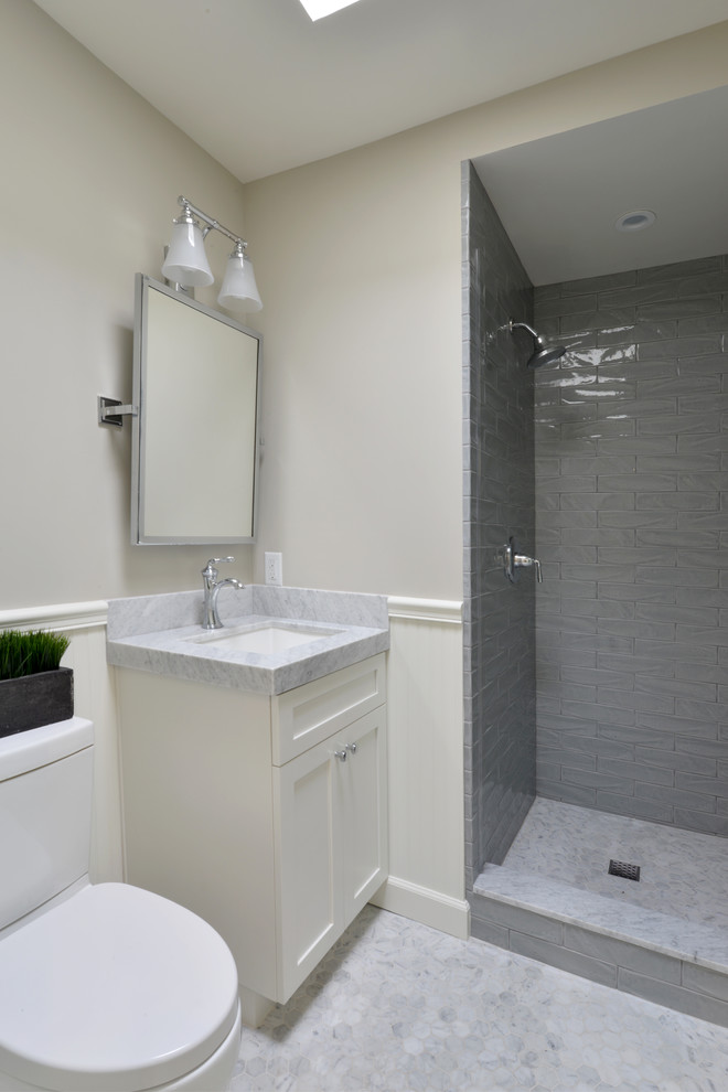 Inredning av ett maritimt litet badrum med dusch, med skåp i shakerstil, vita skåp, en dusch i en alkov, en toalettstol med hel cisternkåpa, grå kakel, tunnelbanekakel, vita väggar, ett undermonterad handfat, marmorbänkskiva och mosaikgolv