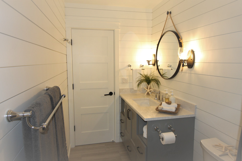 Photo of a medium sized beach style family bathroom in Seattle with shaker cabinets, grey cabinets, an alcove bath, a shower/bath combination, a two-piece toilet, white tiles, white walls, porcelain flooring, a submerged sink, engineered stone worktops, grey floors, a shower curtain and white worktops.