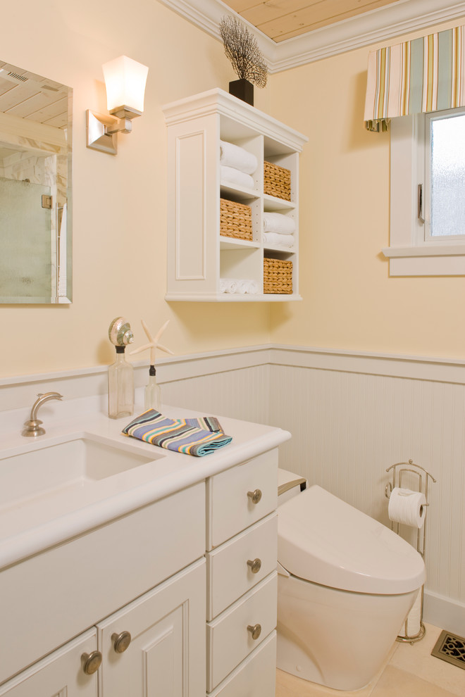 Maritimes Badezimmer mit profilierten Schrankfronten, weißen Schränken, Eckdusche, Bidet, gelber Wandfarbe, Kalkstein und Mineralwerkstoff-Waschtisch in Los Angeles