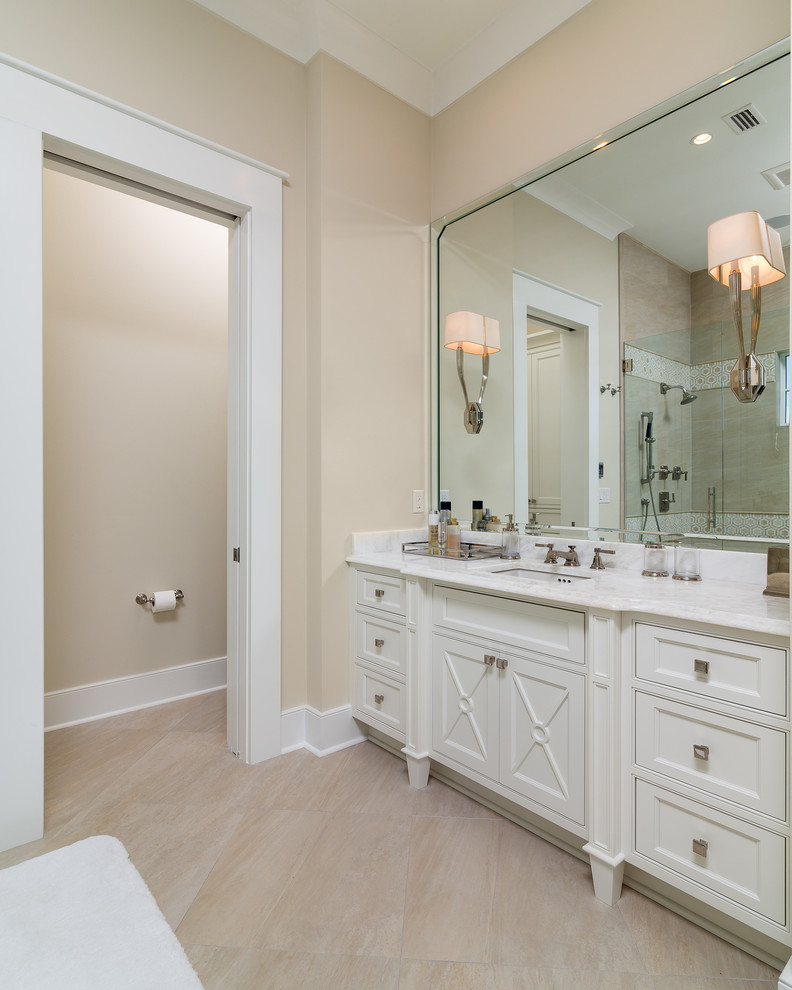 Example of a large beach style master limestone floor corner shower design in Birmingham with recessed-panel cabinets, white cabinets, marble countertops, an undermount tub, a two-piece toilet, beige walls and an undermount sink