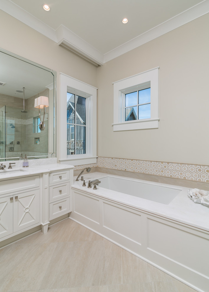 Inspiration for a large coastal master limestone floor corner shower remodel in Birmingham with recessed-panel cabinets, white cabinets, an undermount tub, a two-piece toilet, beige walls, an undermount sink and marble countertops