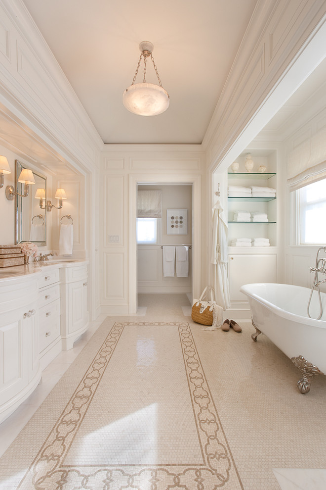 Esempio di una stanza da bagno classica con ante bianche, vasca con piedi a zampa di leone, piastrelle beige, pareti bianche, lavabo sottopiano e ante con bugna sagomata