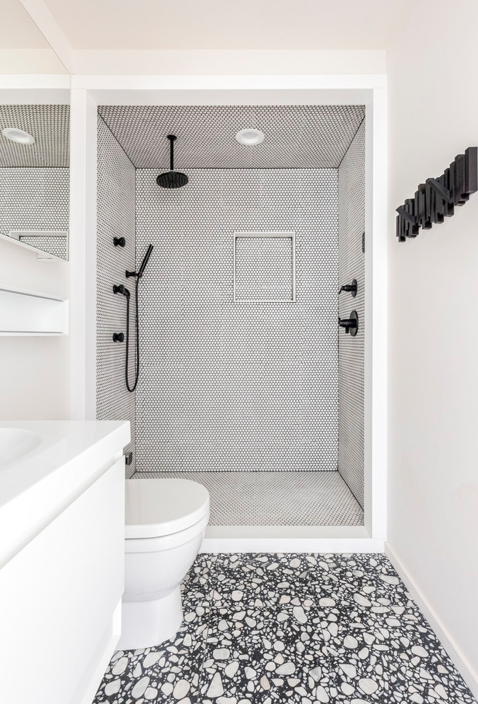 На фото: ванная комната среднего размера в современном стиле с плоскими фасадами, белыми фасадами, душем в нише, белой плиткой, плиткой мозаикой, белыми стенами, душевой кабиной, разноцветным полом, белой столешницей, раздельным унитазом, полом из керамической плитки, накладной раковиной, столешницей из искусственного камня и открытым душем с