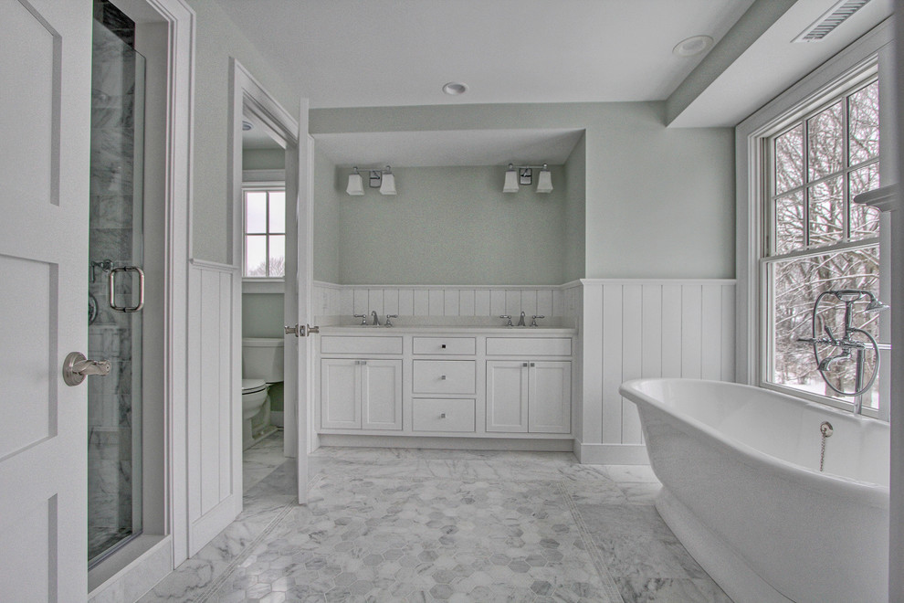 This is an example of a medium sized beach style ensuite bathroom in New York with a submerged sink, shaker cabinets, white cabinets, marble worktops, a freestanding bath, a two-piece toilet, white tiles, grey walls and marble flooring.
