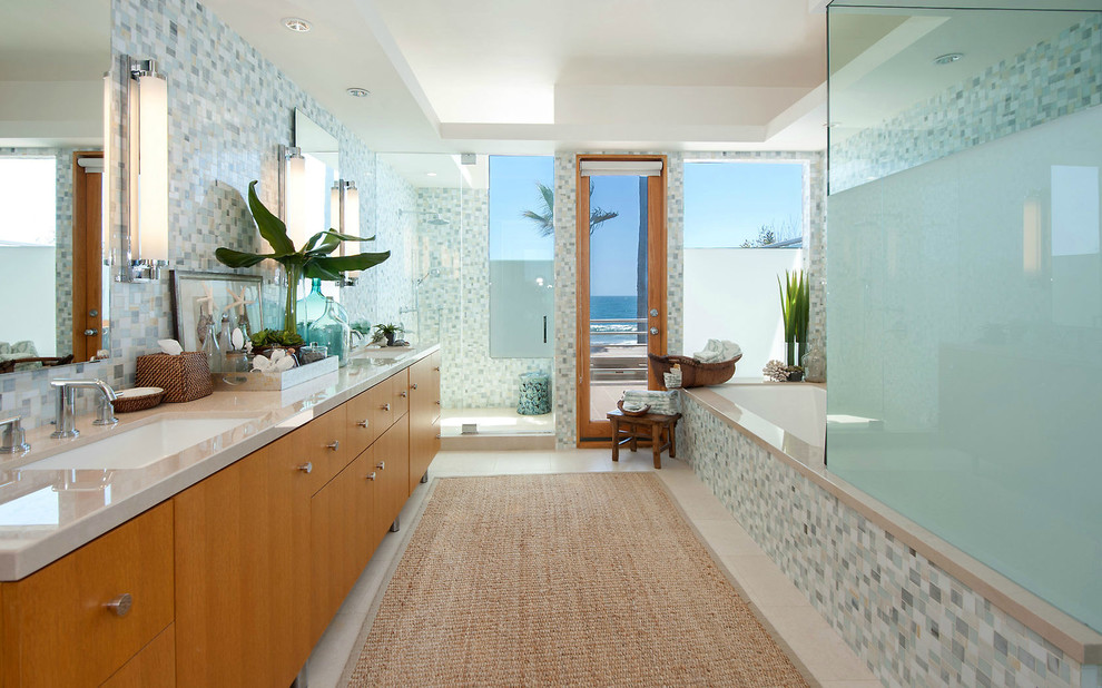 ロサンゼルスにあるビーチスタイルのおしゃれなお風呂の窓 (アンダーカウンター洗面器、フラットパネル扉のキャビネット、中間色木目調キャビネット、アンダーマウント型浴槽、アルコーブ型シャワー、青いタイル、モザイクタイル) の写真