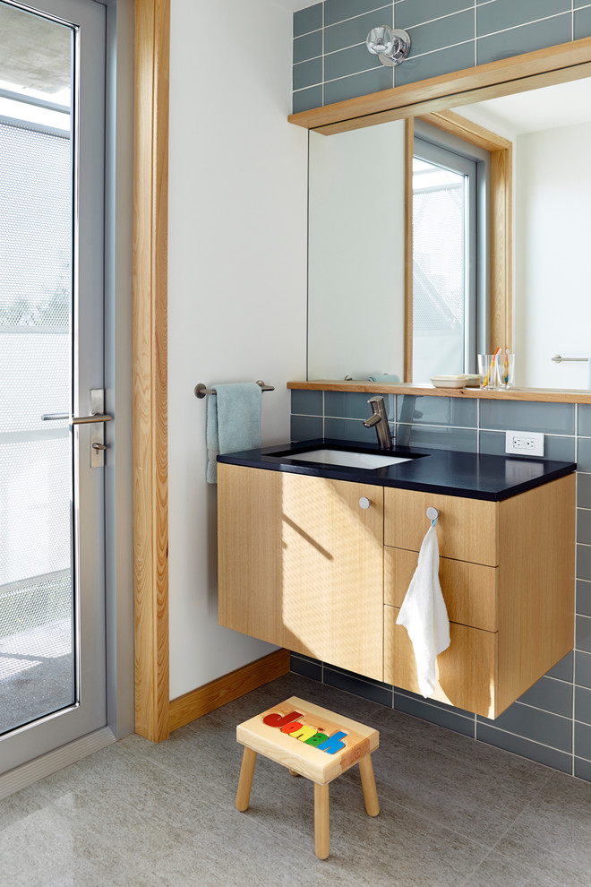 Foto de cuarto de baño marinero con lavabo bajoencimera, armarios con paneles lisos, puertas de armario de madera clara y baldosas y/o azulejos grises