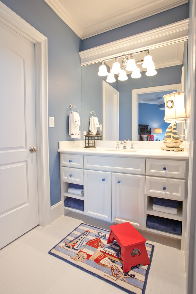 Cette photo montre une grande salle de bain bord de mer pour enfant avec un lavabo posé, un placard avec porte à panneau encastré, des portes de placard blanches, un plan de toilette en granite, un carrelage blanc, des carreaux de porcelaine, un mur bleu et un sol en carrelage de porcelaine.