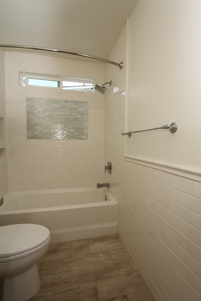 Inredning av ett maritimt badrum, med vita skåp, en dusch/badkar-kombination, en toalettstol med hel cisternkåpa, vit kakel, tunnelbanekakel, vita väggar och bänkskiva i kvartsit