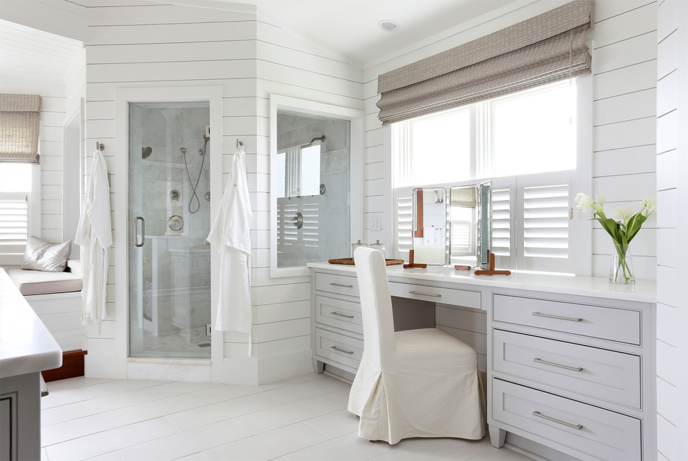 Cette photo montre une salle de bain principale et grise et blanche bord de mer avec des portes de placard grises, une douche d'angle, un carrelage gris, un mur blanc, parquet peint, un placard à porte shaker et une fenêtre.