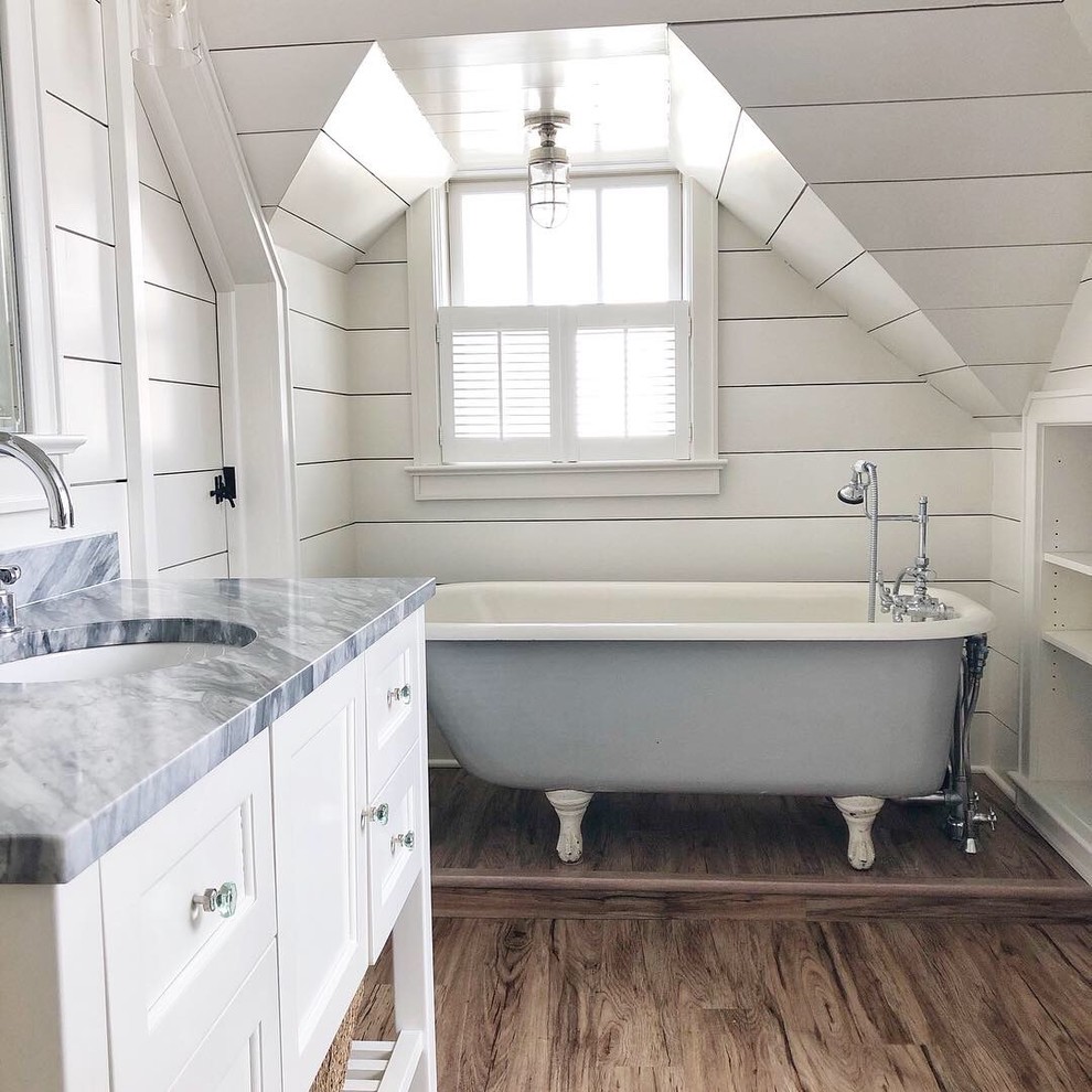 Bild på ett mellanstort maritimt grå grått en-suite badrum, med ett badkar med tassar, vita skåp, vita väggar, mellanmörkt trägolv, ett undermonterad handfat, brunt golv och luckor med infälld panel