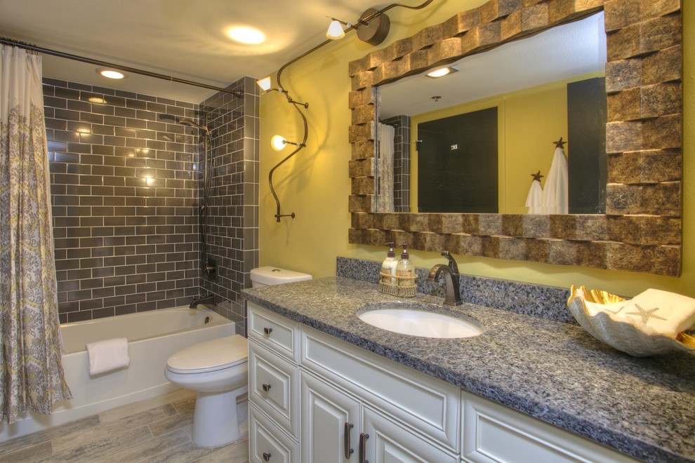 Cette image montre une salle de bain ethnique avec un lavabo encastré, des portes de placard blanches, un plan de toilette en granite, une baignoire en alcôve, un combiné douche/baignoire, WC séparés et un carrelage gris.