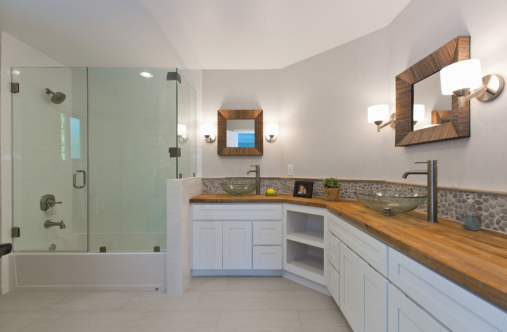 Diseño de cuarto de baño principal costero de tamaño medio con puertas de armario blancas, bañera esquinera, combinación de ducha y bañera, paredes blancas, lavabo tipo consola y encimera de madera