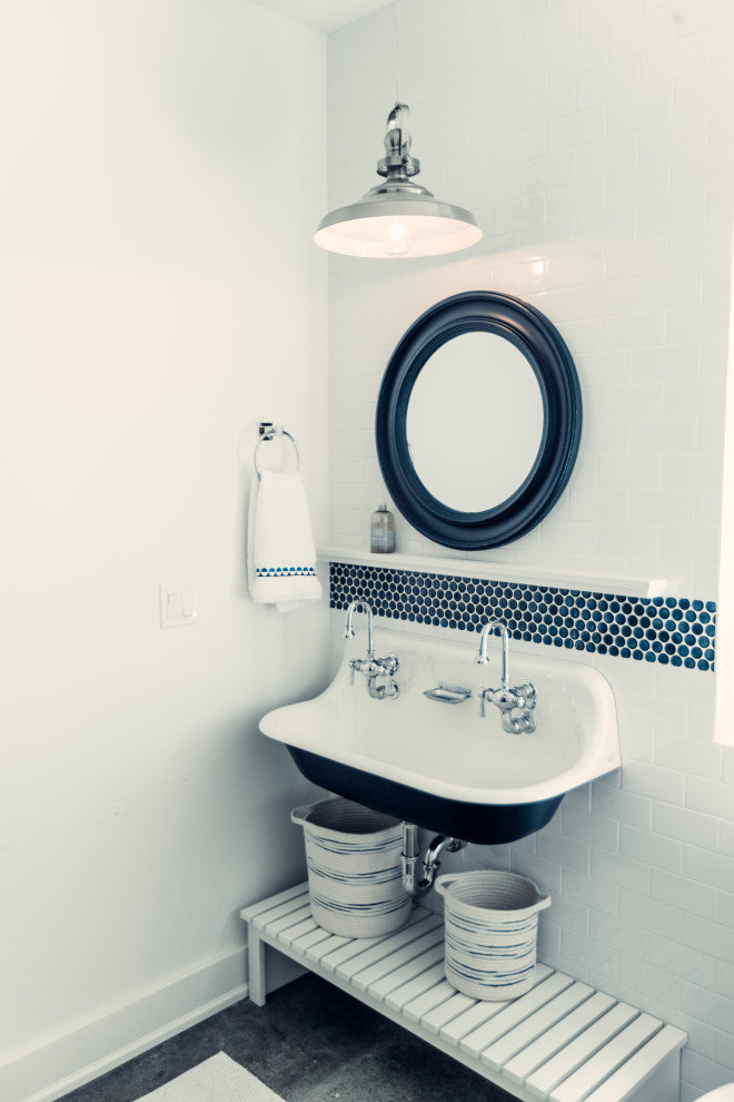 Inredning av ett maritimt mellanstort badrum för barn, med vita skåp, en toalettstol med separat cisternkåpa, blå kakel, glaskakel, vita väggar, betonggolv, ett avlångt handfat och dusch med gångjärnsdörr