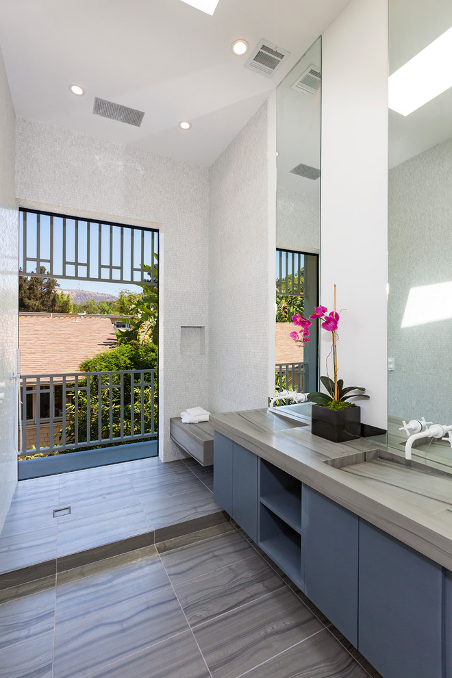 Modernes Badezimmer mit integriertem Waschbecken, flächenbündigen Schrankfronten, blauen Schränken, offener Dusche, weißen Fliesen, Mosaikfliesen, weißer Wandfarbe, Kalkstein, offener Dusche und grauer Waschtischplatte in Los Angeles