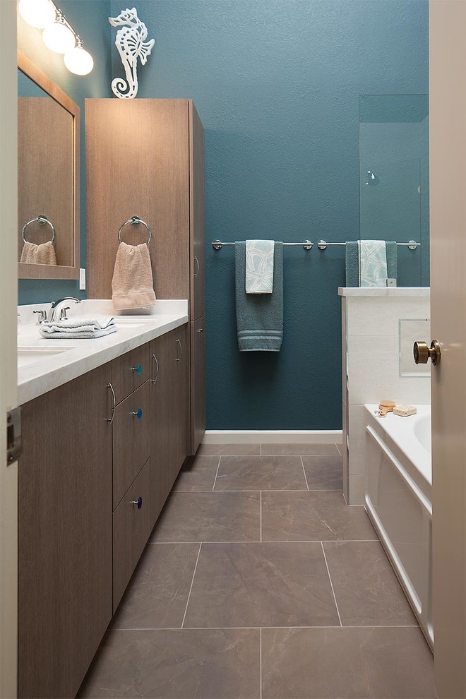Exemple d'une grande salle de bain principale bord de mer en bois brun avec un lavabo encastré, un placard à porte plane, un plan de toilette en surface solide, une baignoire en alcôve, un combiné douche/baignoire, WC séparés, un carrelage gris, des carreaux de porcelaine, un mur bleu et un sol en carrelage de porcelaine.