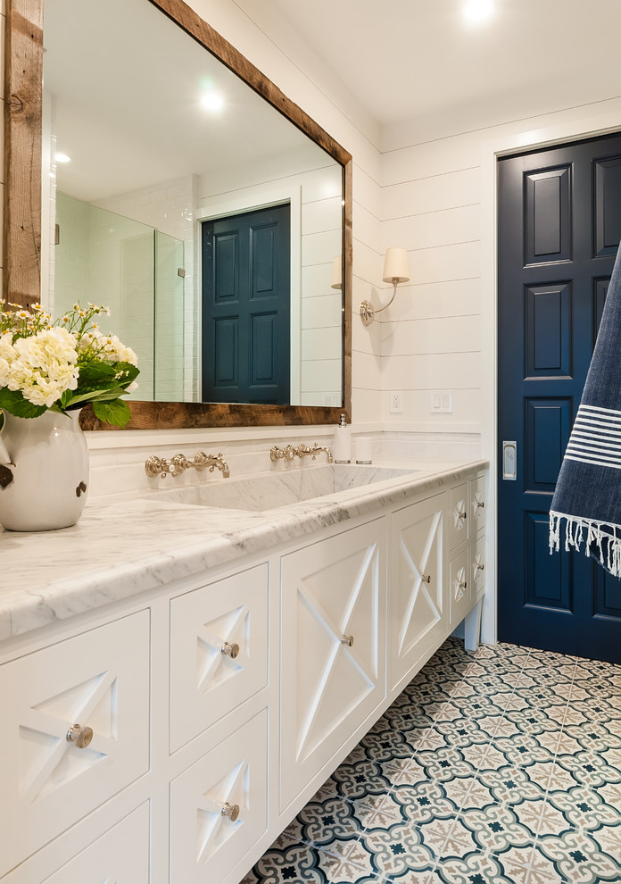 サンディエゴにある高級な広いビーチスタイルのおしゃれなバスルーム (浴槽なし) (落し込みパネル扉のキャビネット、白いキャビネット、白いタイル、白い壁、セメントタイルの床、横長型シンク、大理石の洗面台、青い床、白い洗面カウンター) の写真