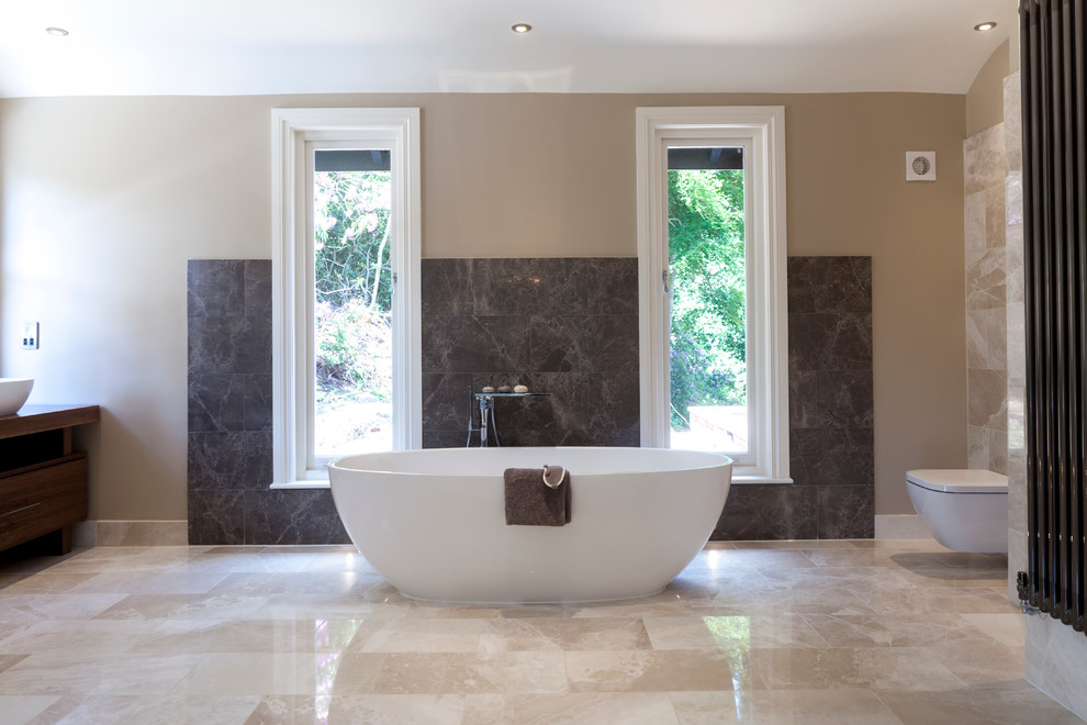 Inspiration for a large contemporary ensuite bathroom in Cheshire with a console sink, flat-panel cabinets, dark wood cabinets, wooden worktops, a freestanding bath, a walk-in shower, a wall mounted toilet, beige walls and marble flooring.