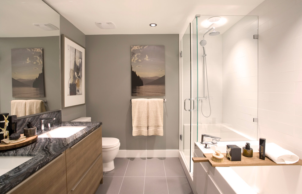 Modern inredning av ett badrum, med ett undermonterad handfat, släta luckor, skåp i mellenmörkt trä, marmorbänkskiva, en dusch i en alkov, en toalettstol med separat cisternkåpa, vit kakel och keramikplattor