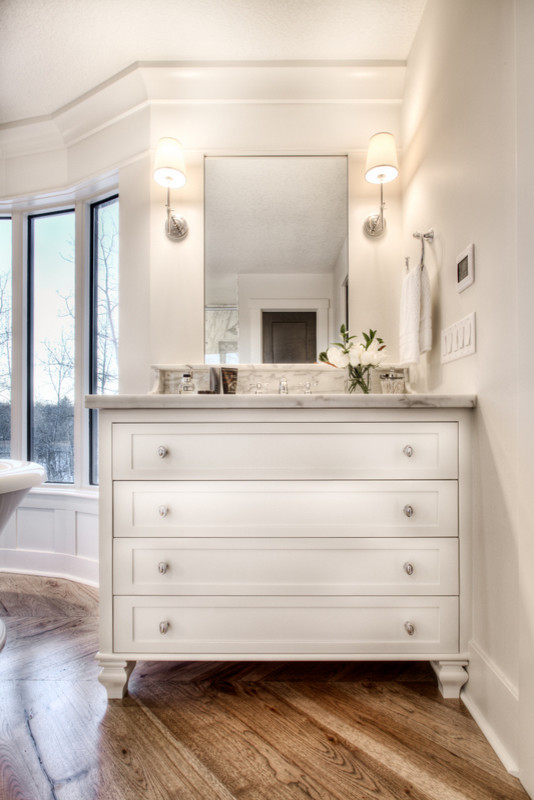 Example of a large classic master medium tone wood floor freestanding bathtub design in Calgary with an undermount sink, furniture-like cabinets, white cabinets, marble countertops and white walls