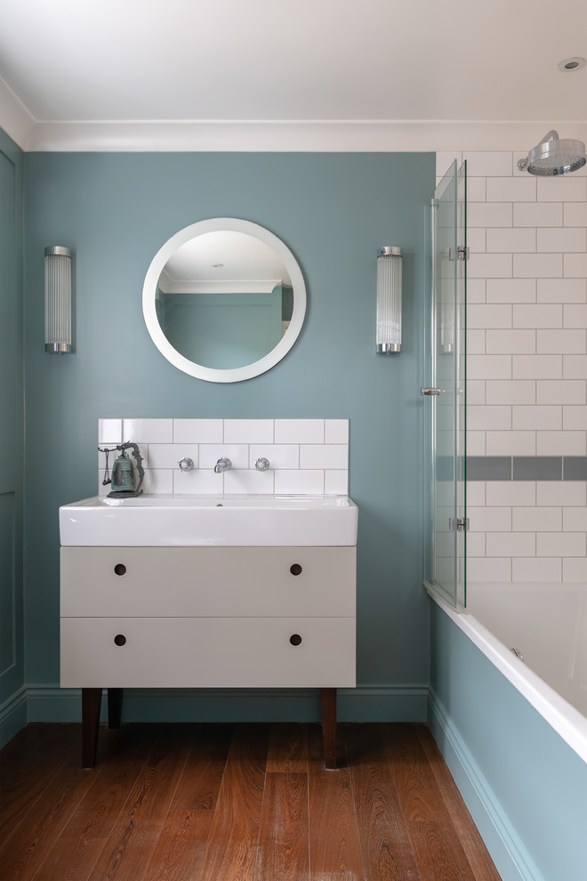 Идея дизайна: ванная комната в современном стиле с серыми фасадами, ванной в нише, душем над ванной, серой плиткой, белой плиткой, плиткой кабанчик, синими стенами, паркетным полом среднего тона, монолитной раковиной, белой столешницей, зеркалом с подсветкой и плоскими фасадами