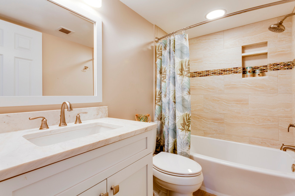タンパにあるお手頃価格の中くらいなトランジショナルスタイルのおしゃれなバスルーム (浴槽なし) (シェーカースタイル扉のキャビネット、白いキャビネット、アルコーブ型浴槽、シャワー付き浴槽	、分離型トイレ、ベージュのタイル、トラバーチンタイル、ベージュの壁、淡色無垢フローリング、アンダーカウンター洗面器、大理石の洗面台、ベージュの床、シャワーカーテン) の写真