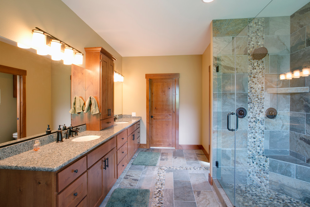 Large rustic ensuite bathroom in Seattle with a submerged sink, shaker cabinets, medium wood cabinets, granite worktops, a built-in bath, a double shower, a one-piece toilet, multi-coloured tiles, stone tiles, beige walls and pebble tile flooring.