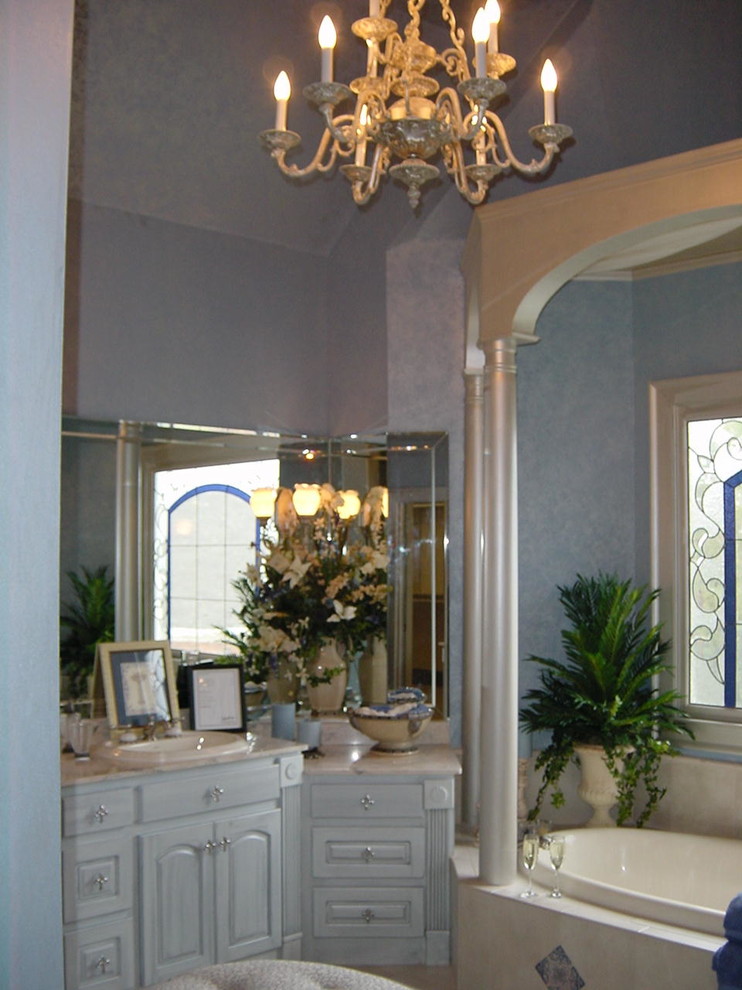 Diseño de cuarto de baño principal romántico de tamaño medio con armarios con rebordes decorativos, puertas de armario blancas, bañera encastrada, paredes azules, suelo de travertino, lavabo encastrado y encimera de cuarzo compacto