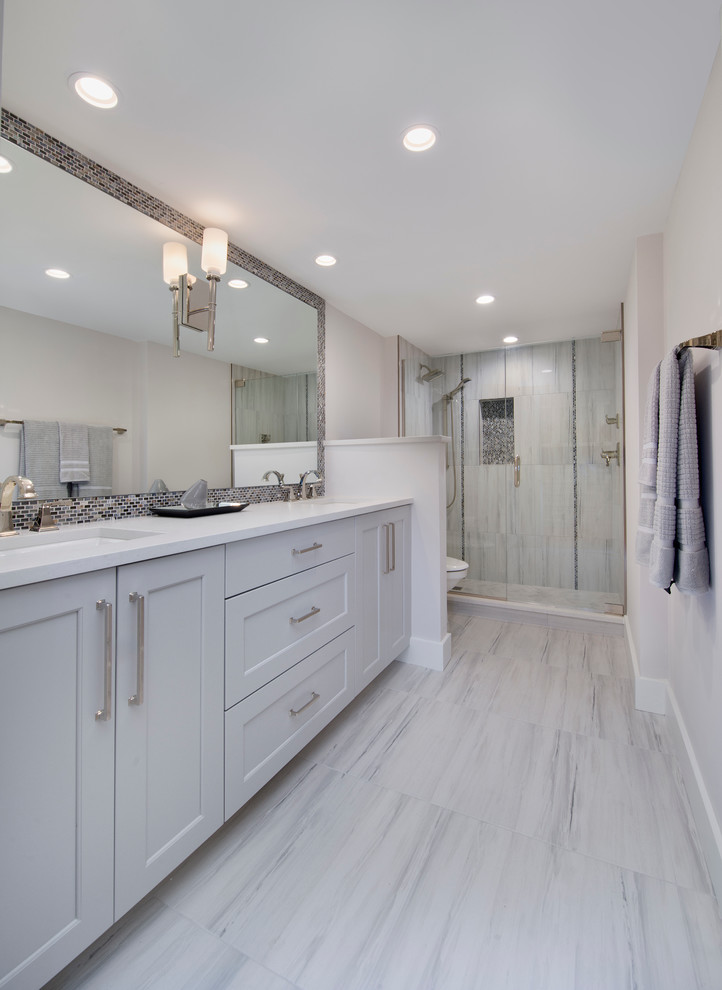 Mid-sized transitional master gray tile and porcelain tile porcelain tile walk-in shower photo in Miami with recessed-panel cabinets, gray cabinets, a two-piece toilet, gray walls, an undermount sink, quartz countertops and a hinged shower door