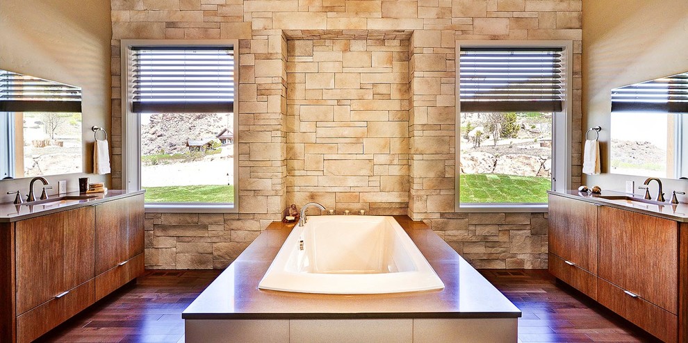 На фото: большая главная ванная комната в стиле фьюжн с плоскими фасадами, темными деревянными фасадами, отдельно стоящей ванной, двойным душем, унитазом-моноблоком, плиткой из известняка, бежевыми стенами, полом из керамогранита, врезной раковиной, столешницей из искусственного кварца, коричневым полом, душем с распашными дверями и серой столешницей с