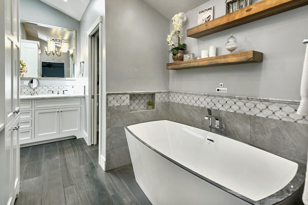 Inredning av ett klassiskt stort vit vitt en-suite badrum, med luckor med profilerade fronter, vita skåp, ett fristående badkar, en dusch i en alkov, en toalettstol med separat cisternkåpa, grå kakel, porslinskakel, grå väggar, klinkergolv i porslin, ett undermonterad handfat, marmorbänkskiva, grått golv och dusch med gångjärnsdörr