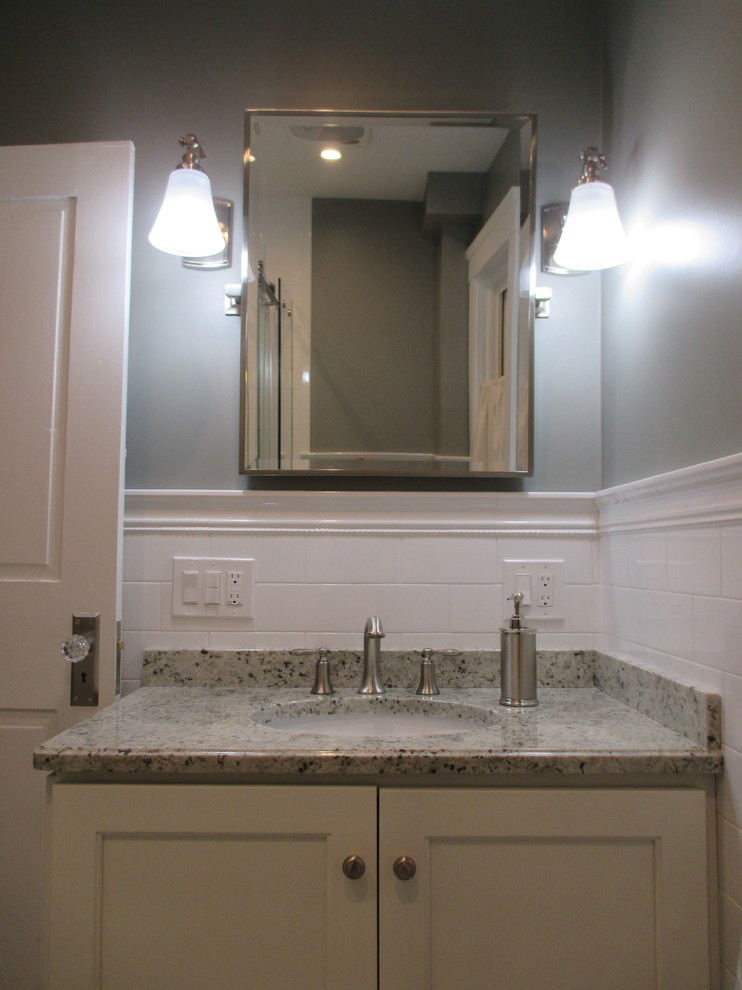 Klassisk inredning av ett litet grå grått badrum med dusch, med vita skåp, en toalettstol med separat cisternkåpa, vit kakel, tunnelbanekakel, grå väggar, granitbänkskiva och skåp i shakerstil