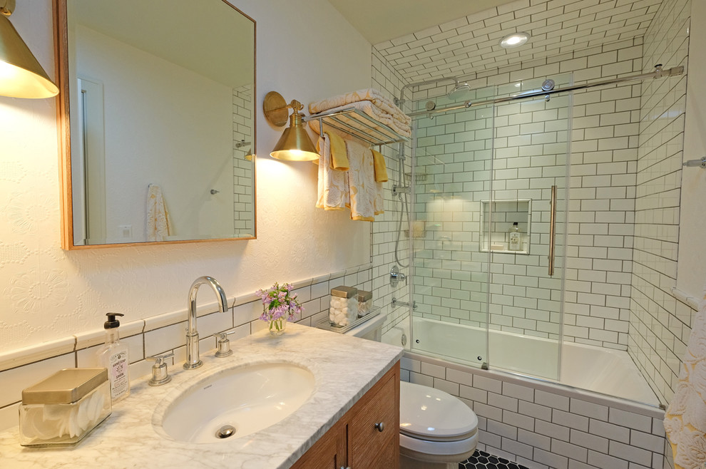 This is an example of a small traditional family bathroom in Chicago with medium wood cabinets, white tiles, white walls, a submerged sink, shaker cabinets, marble worktops, an alcove bath, a one-piece toilet, metro tiles, ceramic flooring and a shower/bath combination.