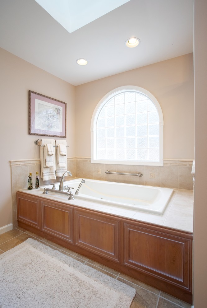 Cette image montre une salle de bain traditionnelle en bois brun avec un placard avec porte à panneau encastré, une baignoire posée et un carrelage beige.