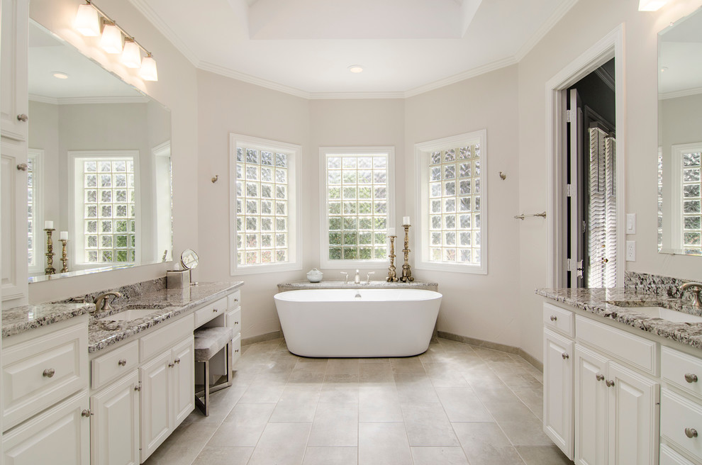 Design ideas for a medium sized traditional ensuite bathroom in Dallas with a submerged sink, raised-panel cabinets, white cabinets, granite worktops, a freestanding bath, a corner shower, a two-piece toilet, grey tiles, porcelain tiles, grey walls and porcelain flooring.