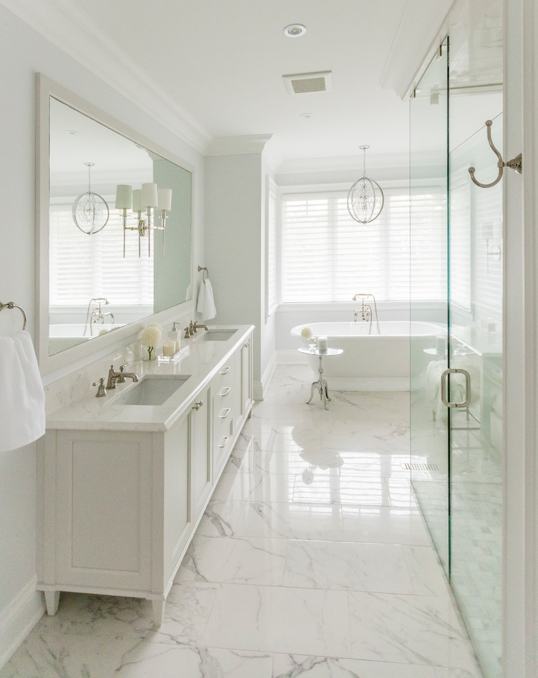Klassisk inredning av ett en-suite badrum, med ett fristående badkar, en kantlös dusch, vit kakel, grå väggar, klinkergolv i porslin, ett undermonterad handfat, bänkskiva i kvarts, vita skåp och luckor med infälld panel