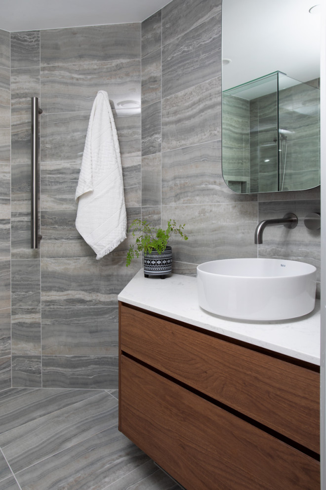 Réalisation d'une petite salle de bain design en bois brun avec WC à poser, un carrelage gris, des carreaux de porcelaine, un mur gris, un sol en carrelage de porcelaine, une vasque, un sol gris, une cabine de douche à porte battante, un plan de toilette blanc, une niche, meuble simple vasque et meuble-lavabo suspendu.