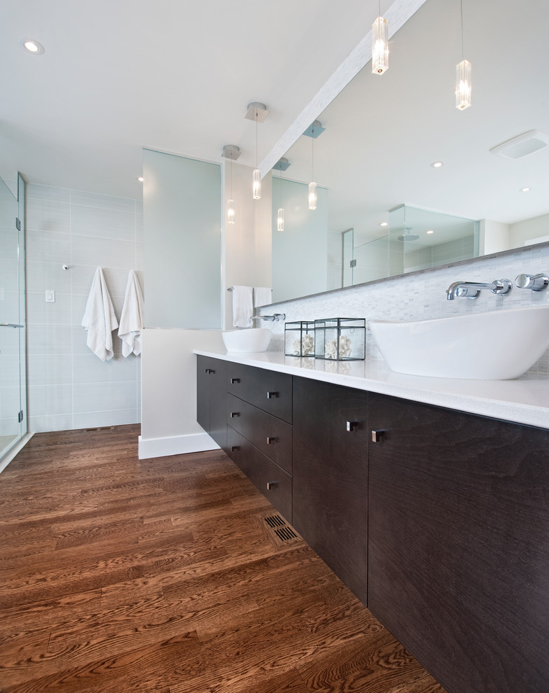 Modern ensuite bathroom in Ottawa with a vessel sink, flat-panel cabinets, dark wood cabinets, engineered stone worktops, a freestanding bath, a built-in shower, a one-piece toilet, white tiles, porcelain tiles, grey walls and medium hardwood flooring.