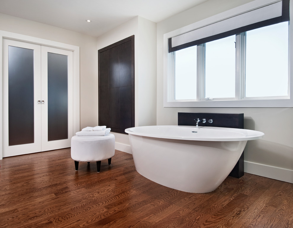 Photo of a modern ensuite bathroom in Ottawa with a vessel sink, flat-panel cabinets, dark wood cabinets, engineered stone worktops, a freestanding bath, a built-in shower, a one-piece toilet, white tiles, porcelain tiles, grey walls and medium hardwood flooring.