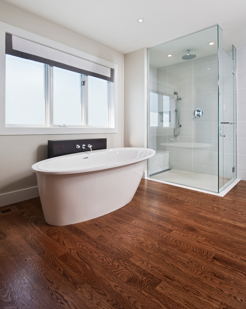This is an example of a modern ensuite bathroom in Ottawa with flat-panel cabinets, dark wood cabinets, a freestanding bath, a built-in shower, white tiles, porcelain tiles, grey walls and medium hardwood flooring.